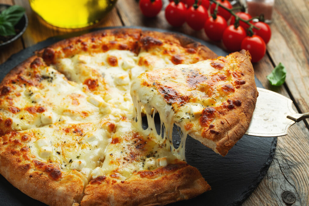 A slice of hot Italian pizza with stretching cheese. Pizza four cheeses with basil on a wooden background. (Foto: banco de imagens)