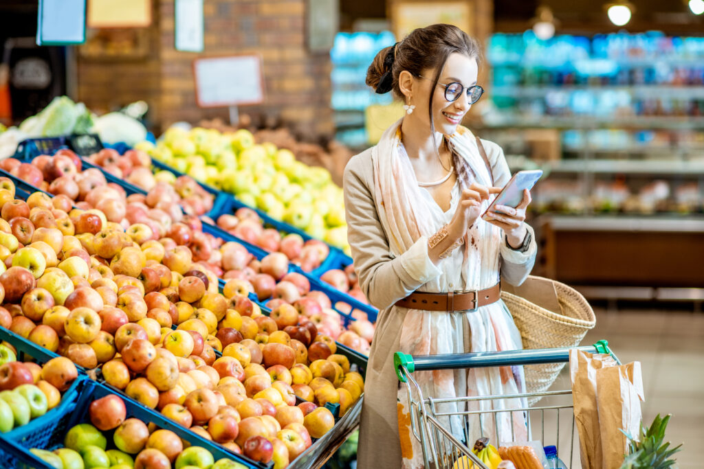 Young woman looking on the shopping list using smartphone while shopping food in the supermarket. (Foto: banco de imagens)