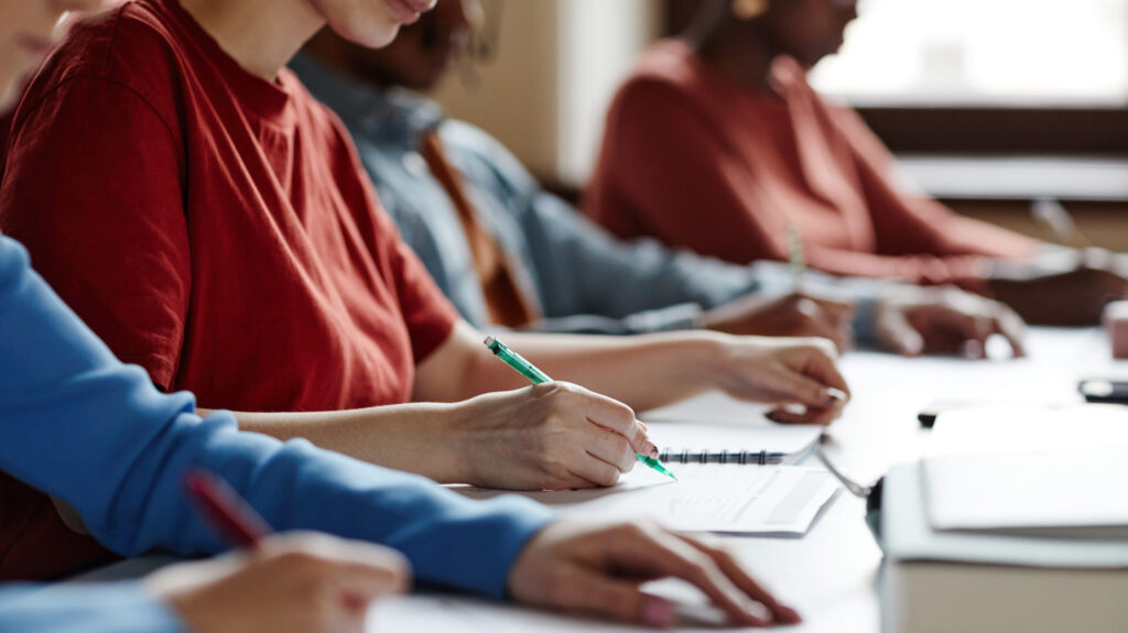 Side view close up of students in row taking notes during lecture in college classroom, copy space. (Foto: banco de imagens)